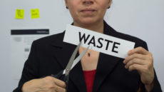 59667727 - female office worker or business woman cuts a piece of paper with the word waste on it as a waste reduction business concept.